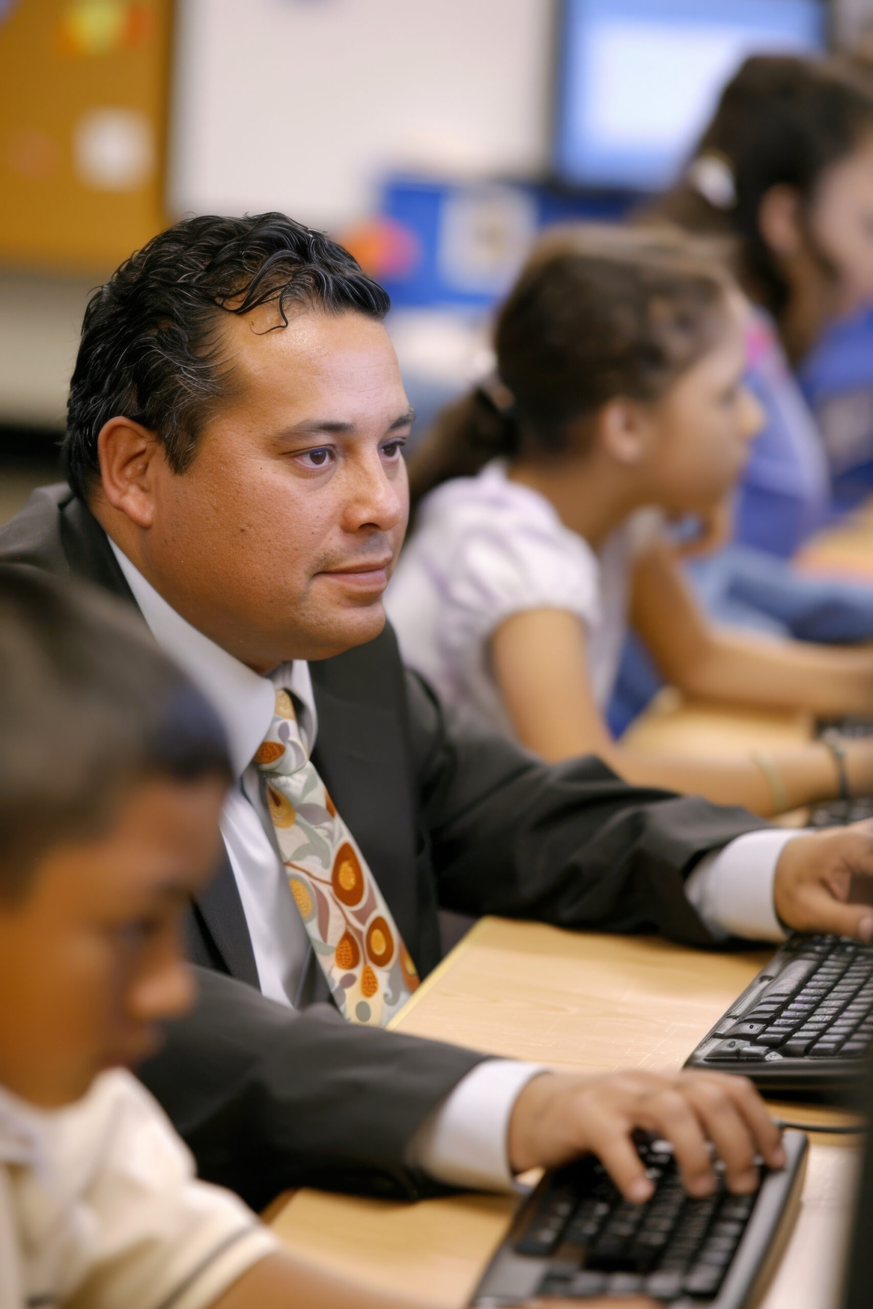 a Latino teacher guiding students in a computer lab